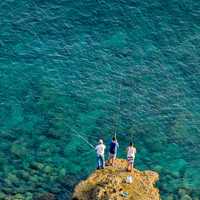 Three people fishing on a rock outcropping