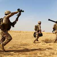 Three US Marines carrying weapons walking across the desert