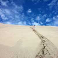 Person with walking stick standing on the sand dunes under blue sky