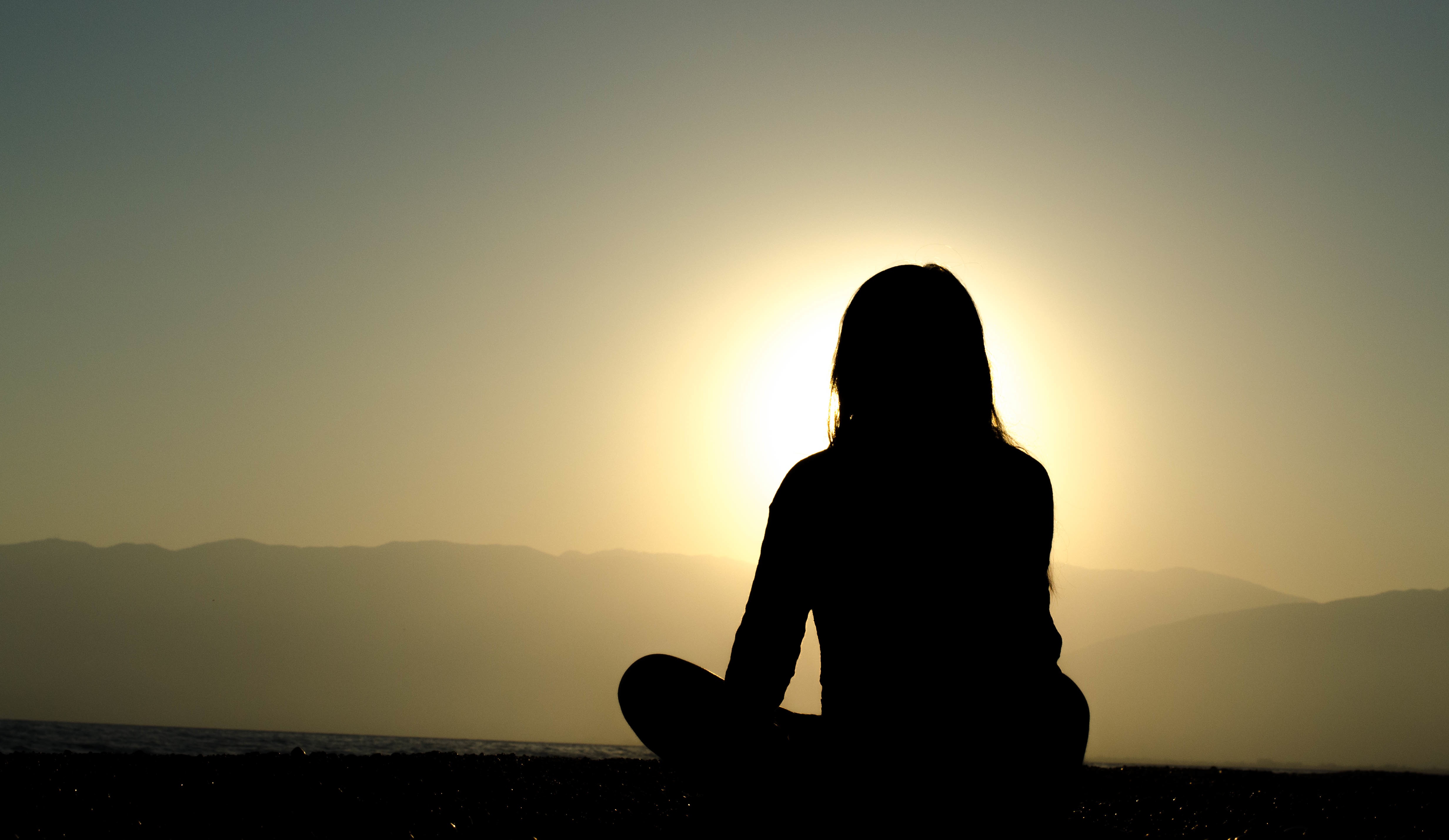 Outline of woman sitting on hill watching the sunset.