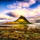 Mountain out of the ocean with clouds over top in Iceland