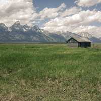 Beautiful Landscape with grassland and Mountains with Cabin under sky and clouds