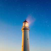 Lighthouse beneath the sky and stars with light on