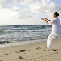 man-dressed-in-white-praticing-tai-chi-on-beasch