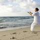 man-dressed-in-white-praticing-tai-chi-on-beasch