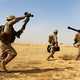 Three US Marines carrying weapons walking across the desert