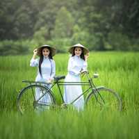 two-asian-girls-riding-a-bicycle-through-a-field