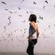 woman-standing-under-flying-flock-of-birds