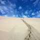 Person with walking stick standing on the sand dunes under blue sky