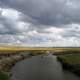 Fisherman standing in the middle of a stream under clouds and sky